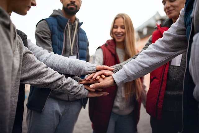 a close up of group of happy community service volunteers stacking hands together outdoors in street