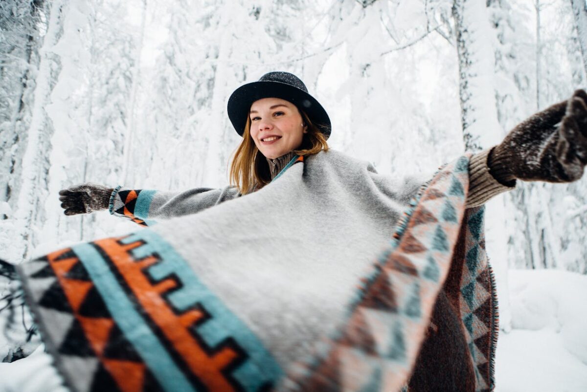 portrait-of-woman-in-hat-and-poncho-in-forest-in-winter