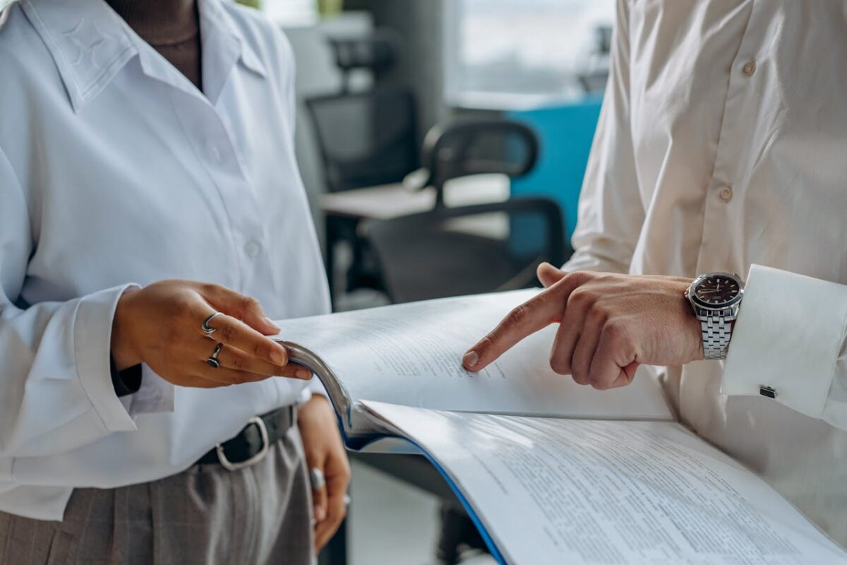 colleagues-standing-in-white-long-sleeve-shirts-discussing-and-reading-a-financial-report